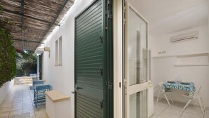 A covered outdoor area with a table and chairs, a green door, and a glass door leading to a room.