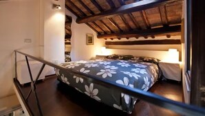 A bedroom with a wooden ceiling, a bed with a floral bedspread, and a nightstand with a lamp. - Loft on Via dei Cappellari, near Campo de' Fiori (Rome)