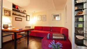 A cozy living room with a red sofa, a small table with a lamp, and shelves with decorative items. - Loft on Via dei Cappellari, near Campo de' Fiori (Rome)