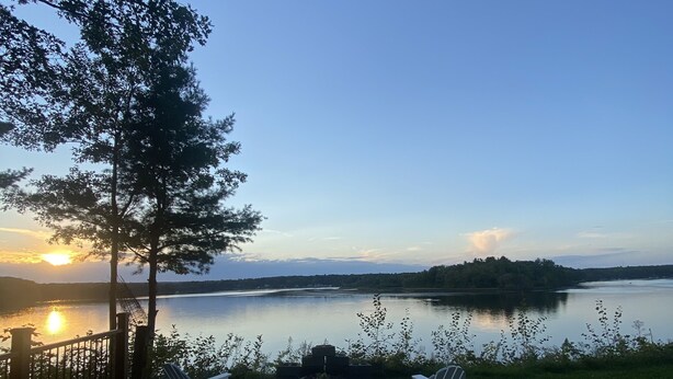 En uteplats med två Adirondack-stolar som är placerade så att de vetter mot en sjö vid solnedgången.