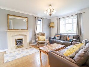 A living room with a fireplace, a sofa, a chair, and a coffee table. - Pencraig (Colwyn Bay)
