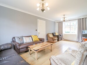 A living room with a brown leather sofa, a wooden coffee table, and a beige armchair. - Pencraig (Colwyn Bay)