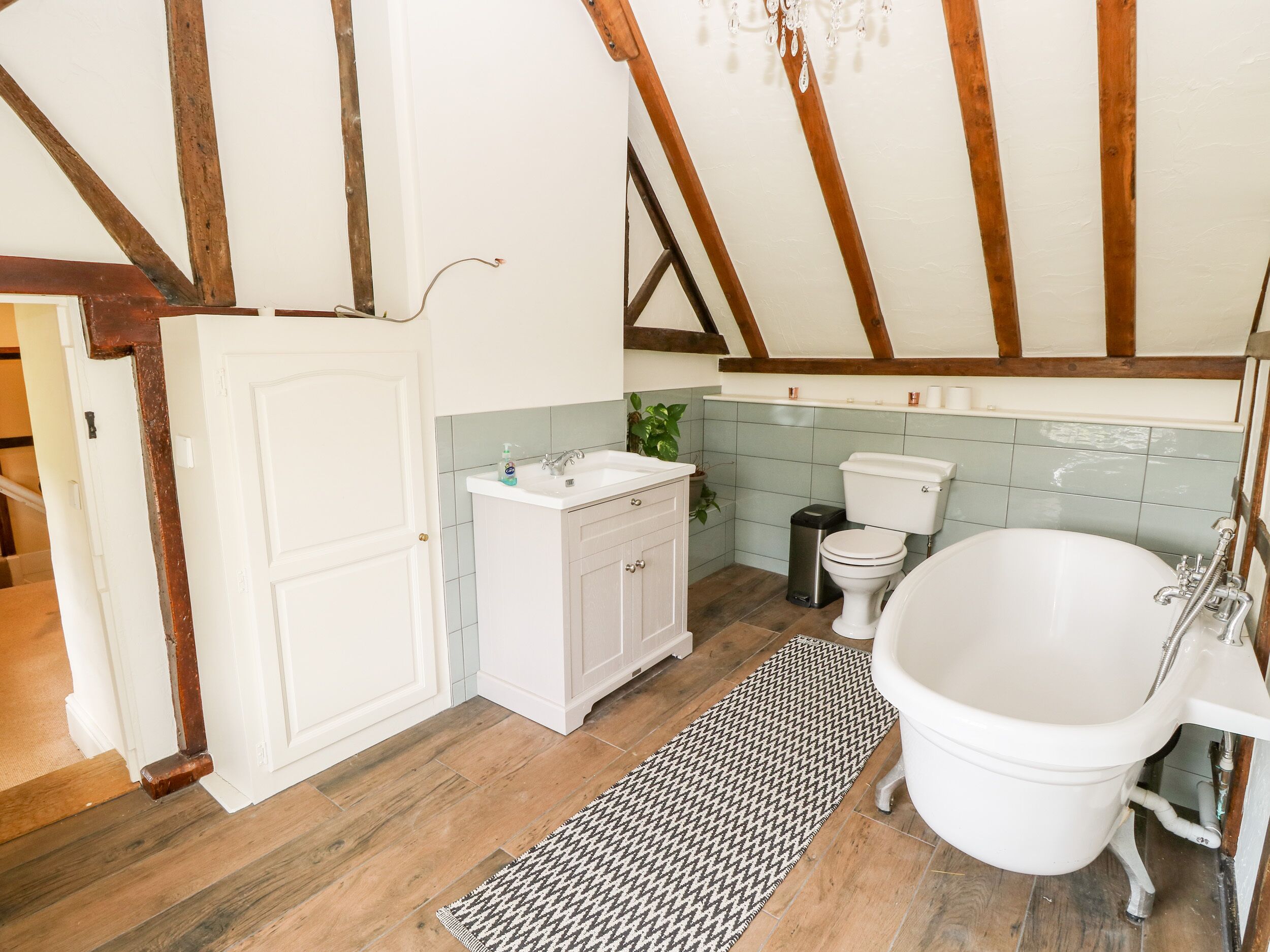 Une salle de bain avec une baignoire blanche, un lavabo et des toilettes. Un tapis à motifs en chevrons recouvre le sol.