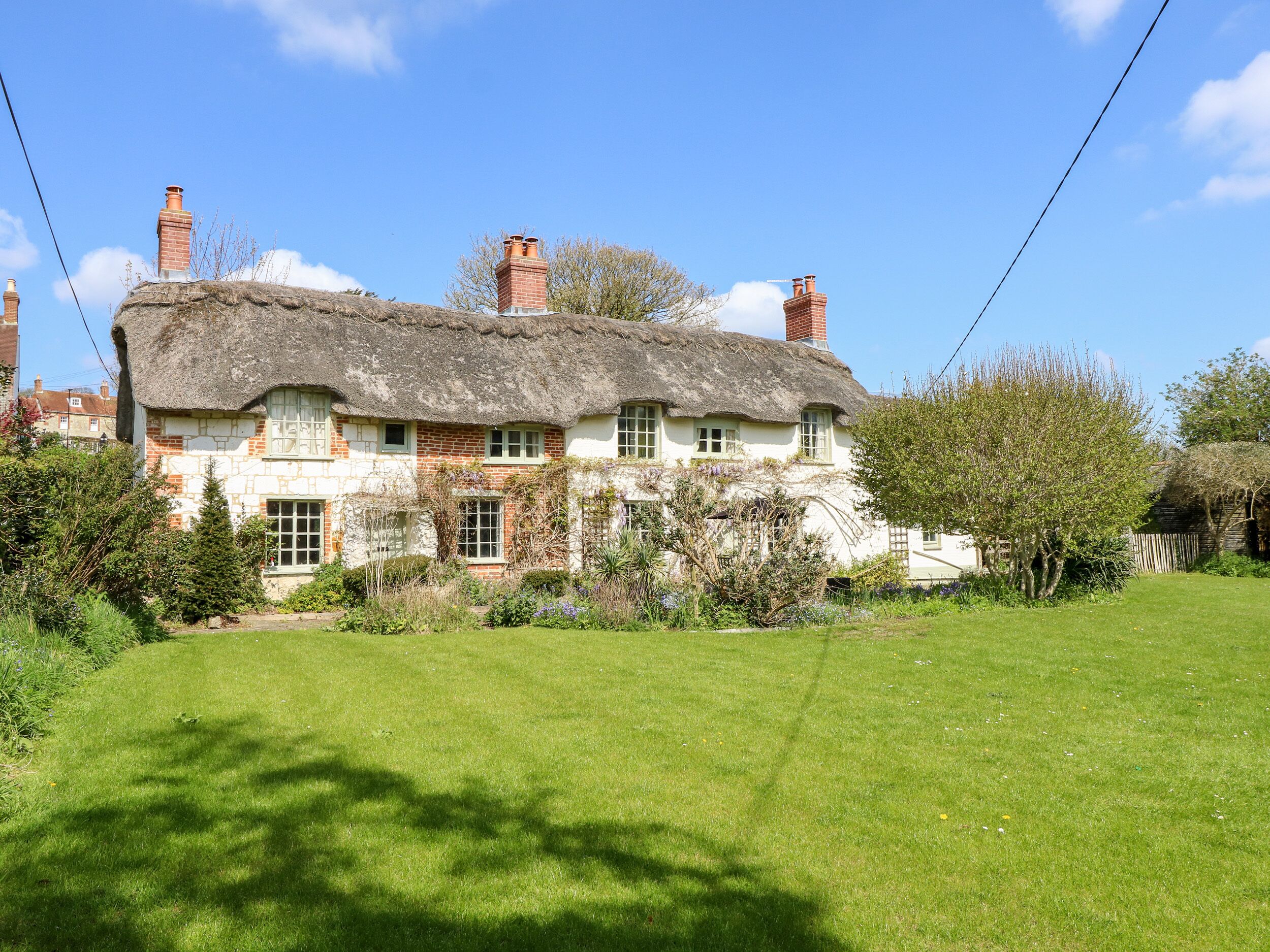 A traditional thatched-roof house with brick walls, surrounded by a well-maintained lawn and garden.