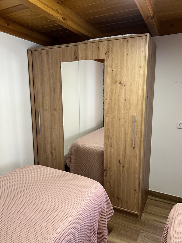 A room with a wooden wardrobe, two beds with pink bedding, and a wooden ceiling. - Rural house with an attic and a pool in Mogán (Mogán)