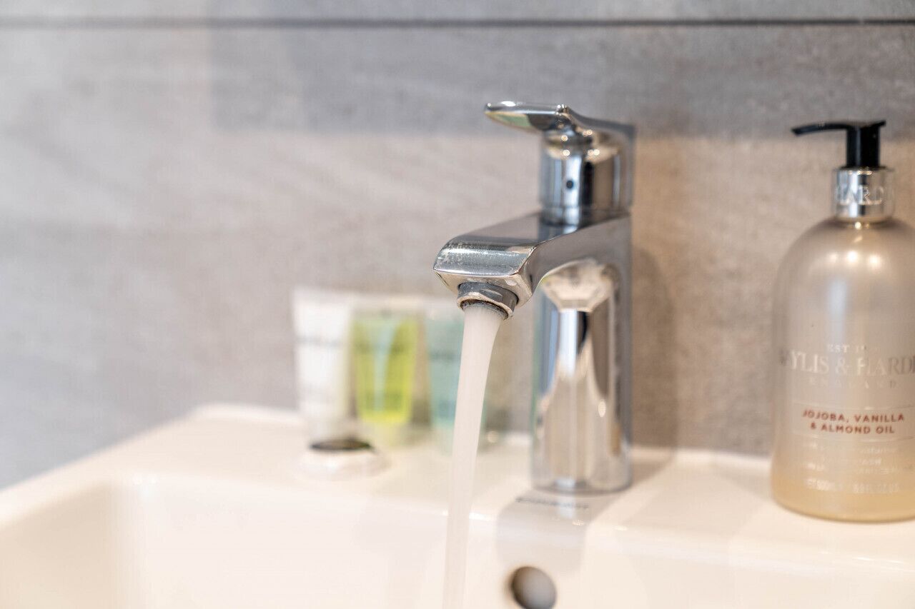 Ein Waschbecken mit fließendem Wasser, einem Seifenspender und einer Ölflasche.