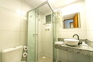 Une salle de bain avec une douche à parois de verre, un lavabo blanc avec un robinet noir et un miroir au-dessus du lavabo.