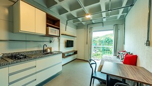Een moderne keuken met een ingebouwde kookplaat, magnetron en televisie. Er is een eethoek met een tafel en stoelen, en een balkon met uitzicht op groen.