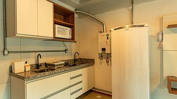 Cozinha com armários brancos, bancada de granito, micro-ondas embutido, aquecedor de água e geladeira.
