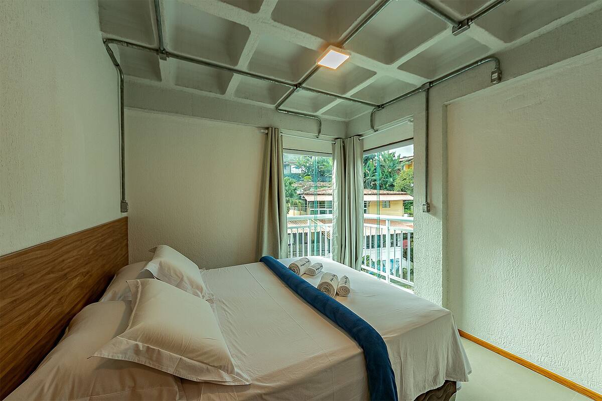 Een hotelkamer met een bed, een raam met gordijnen en uitzicht op gebouwen.