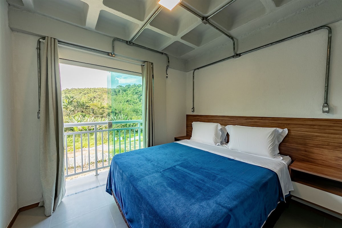 Een slaapkamer met een groot bed, een houten hoofdbord en een balkon met uitzicht op groen.