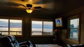 Une chambre avec vue sur l’eau, un ventilateur de plafond et un tableau encadré au mur.