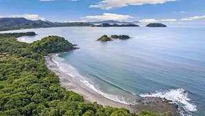 Un paysage côtier comprenant une plage, des zones boisées et de petites îles à l’horizon.