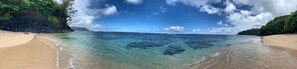 Ein Strand mit klarem türkisblauem Wasser, einem sandigen Ufer und einer felsigen Klippe mit viel Grün.