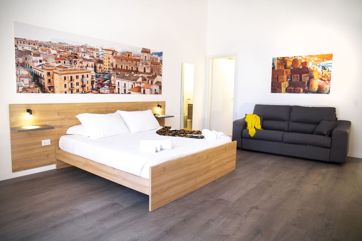 A modern bedroom with a wooden bed, a grey sofa, and two wall-mounted lamps.