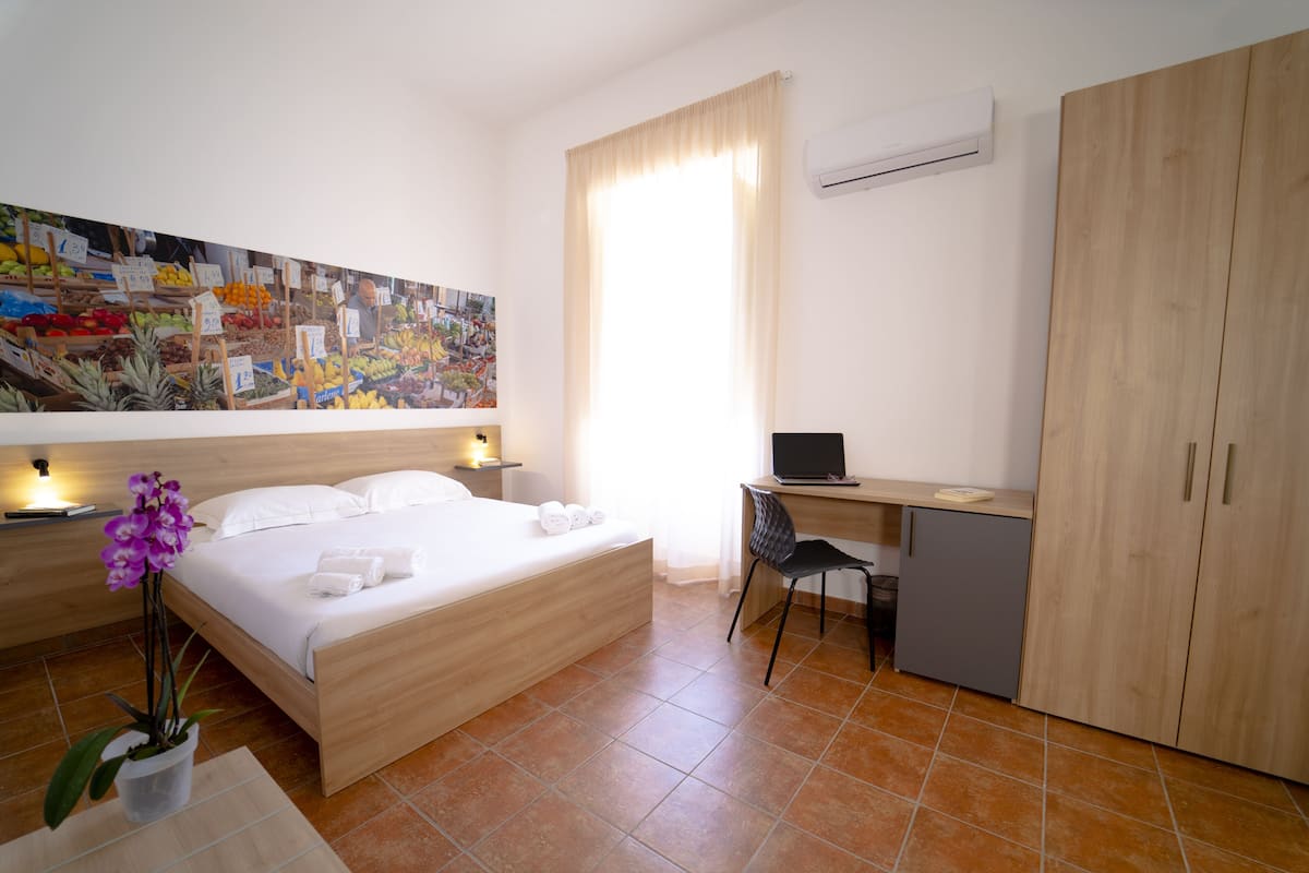 A hotel room with a bed, desk, chair, and a painting on the wall.