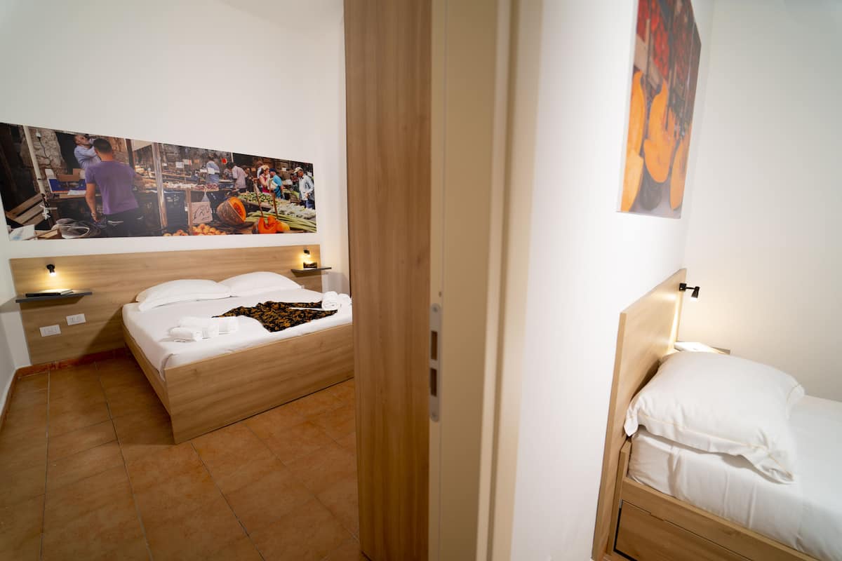 A bedroom with two beds, a wooden headboard, a large painting on the wall, and a tiled floor.
