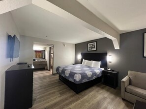 A hotel room with a large bed, a desk, a chair, and a small kitchenette.