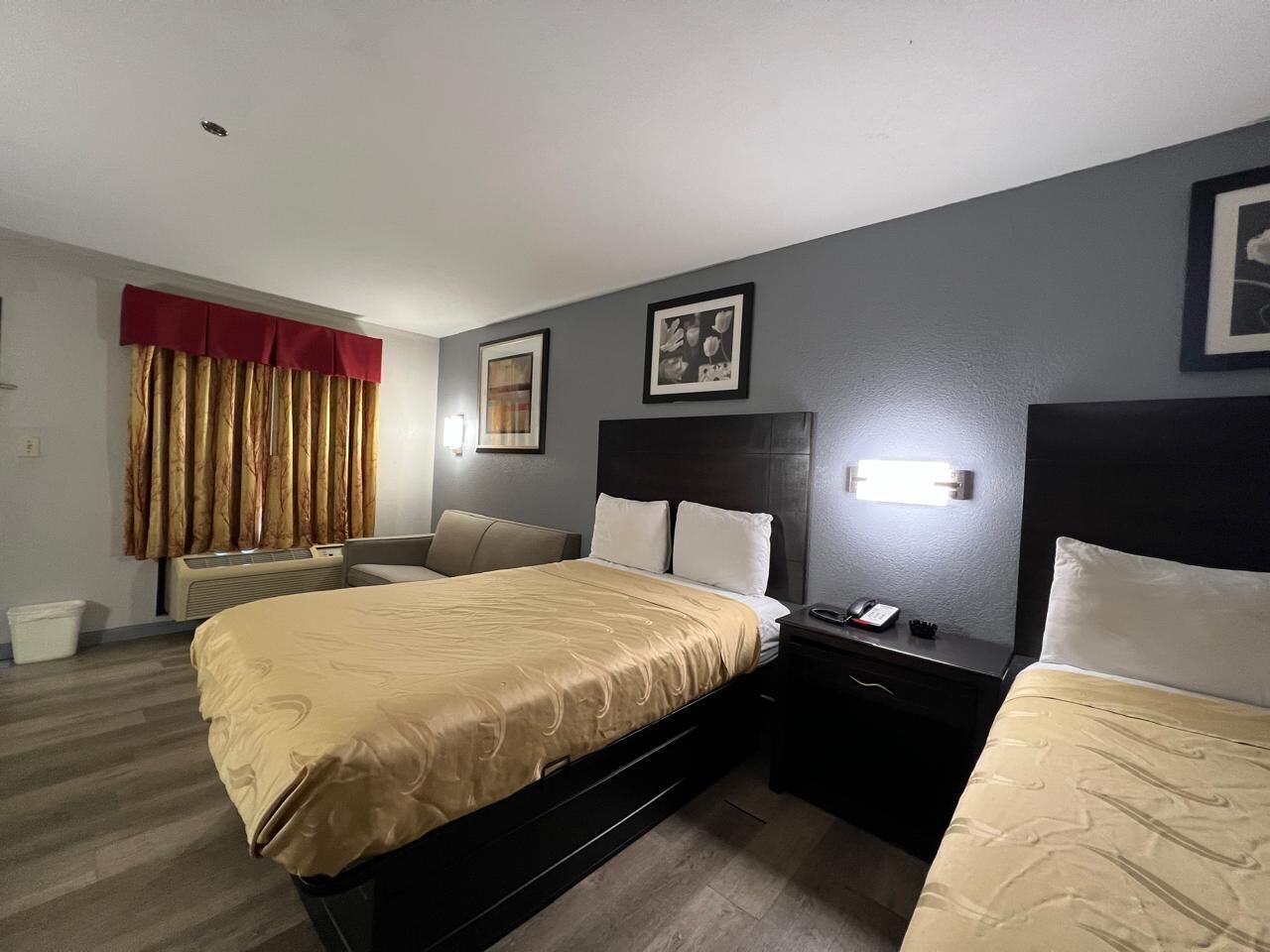 Une chambre d’hôtel avec un grand lit, deux tables de chevet, une chaise, un bureau et une fenêtre avec des rideaux.