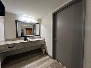 A bathroom with a granite countertop, a sink, a mirror, and a door.