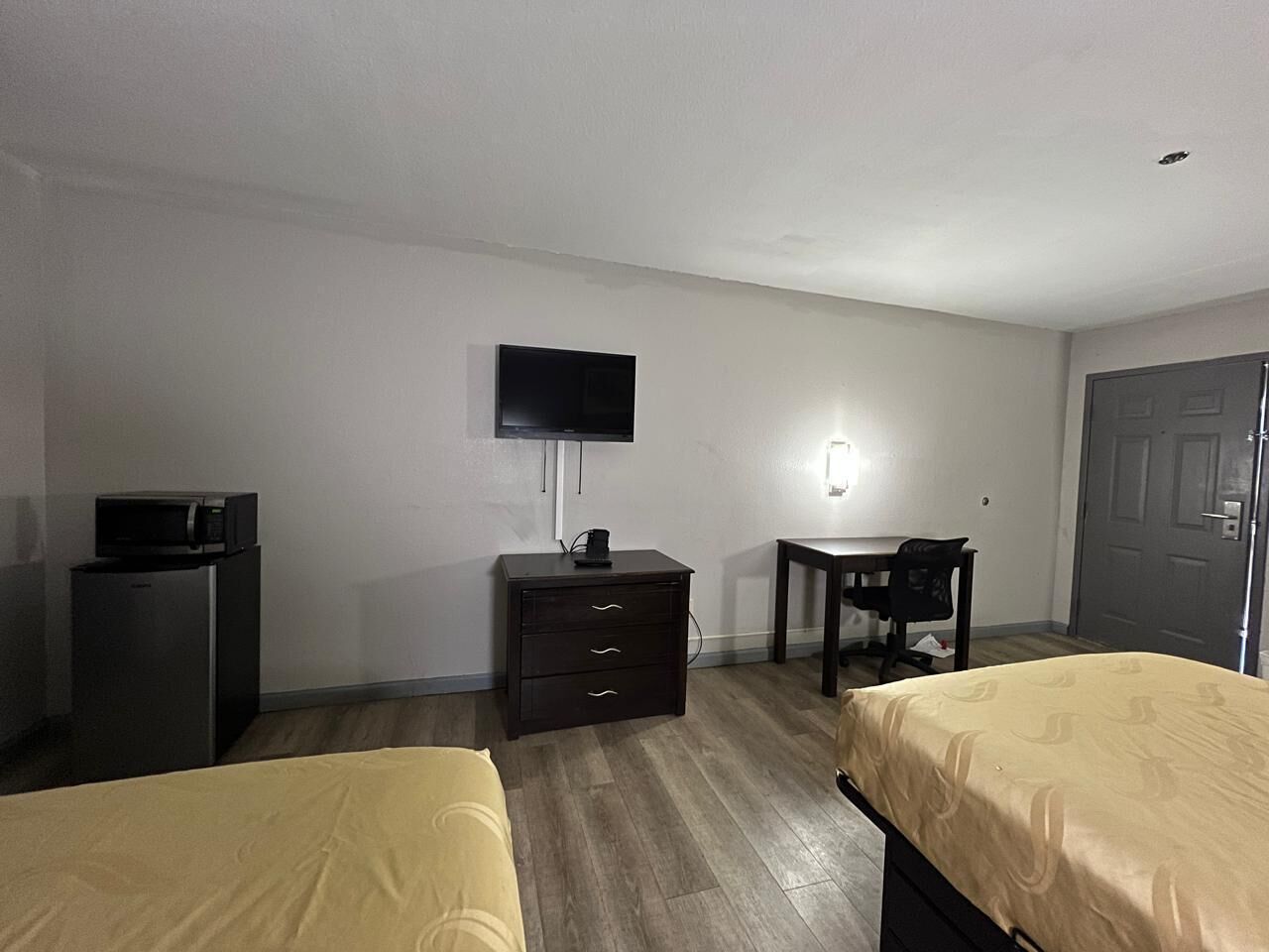 A hotel room with two beds, a desk, a chair, a television, a dresser, and a door.