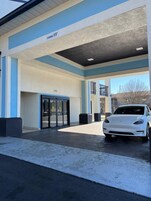 Una estación de carga Tesla con un cartel de altura, una entrada cubierta y un coche blanco estacionado dentro.
