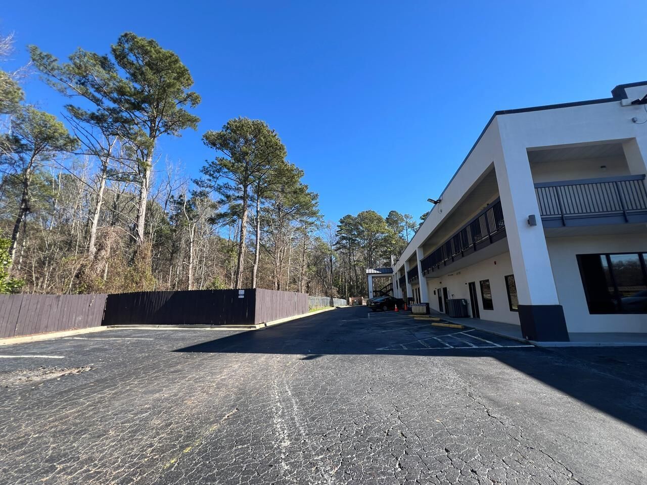 A parking lot with a building featuring a modern design, a fenced area, and trees in the background.