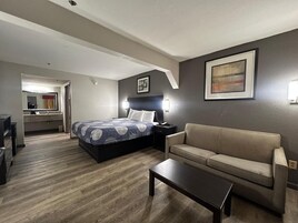 Una habitación de hotel con una cama, un sofá, una mesa de centro y un escritorio con una silla. Se ve un baño al fondo.