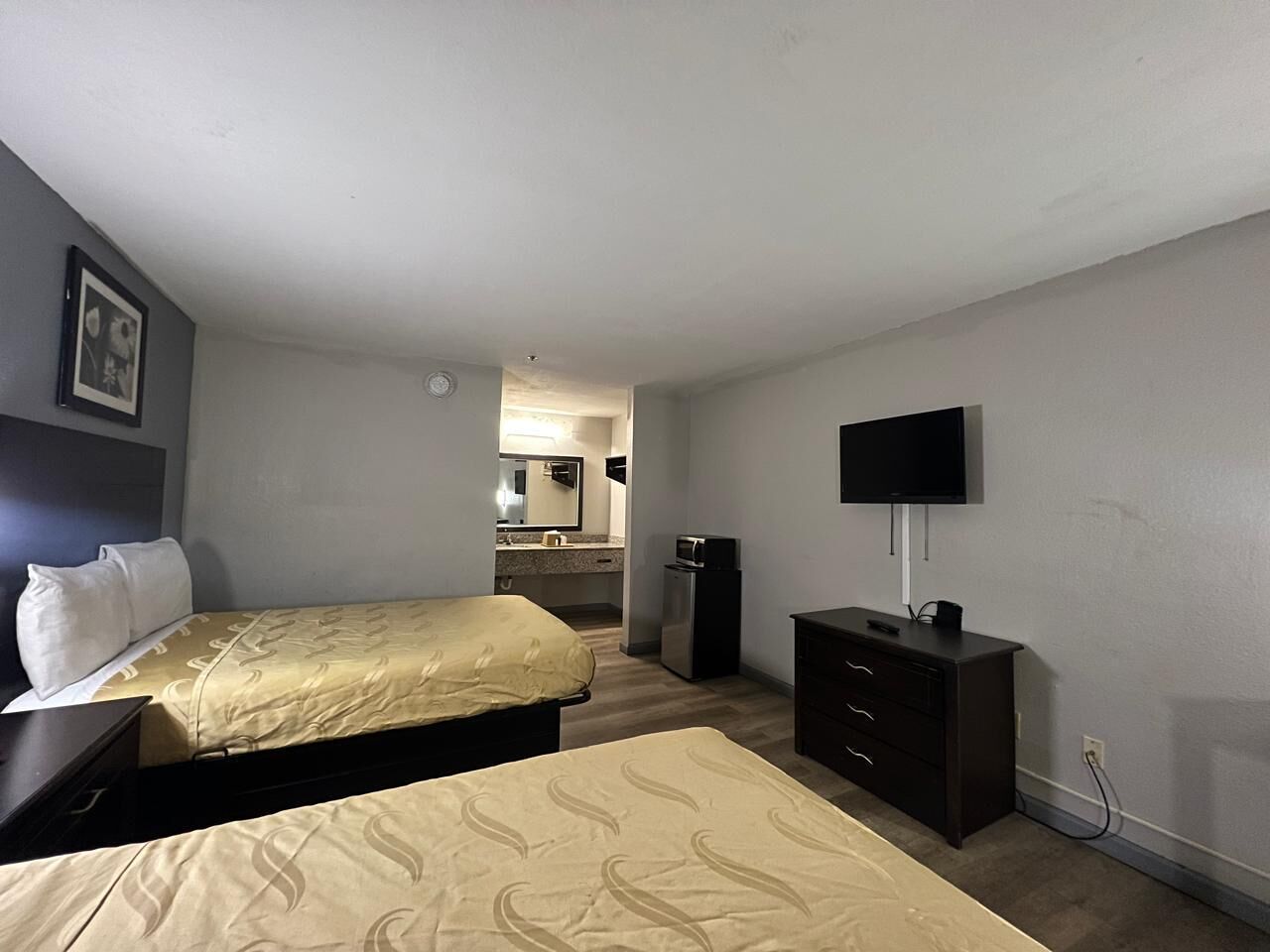 A hotel room with two beds, a TV, a desk, and a small kitchenette.