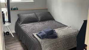 A bedroom with a bed, a window, a shelf with a tissue box, and a door.