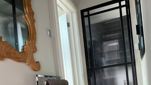 A hallway with a wooden floor, a metal towel rack with a towel, a wooden mirror, and a black-framed door with a window.