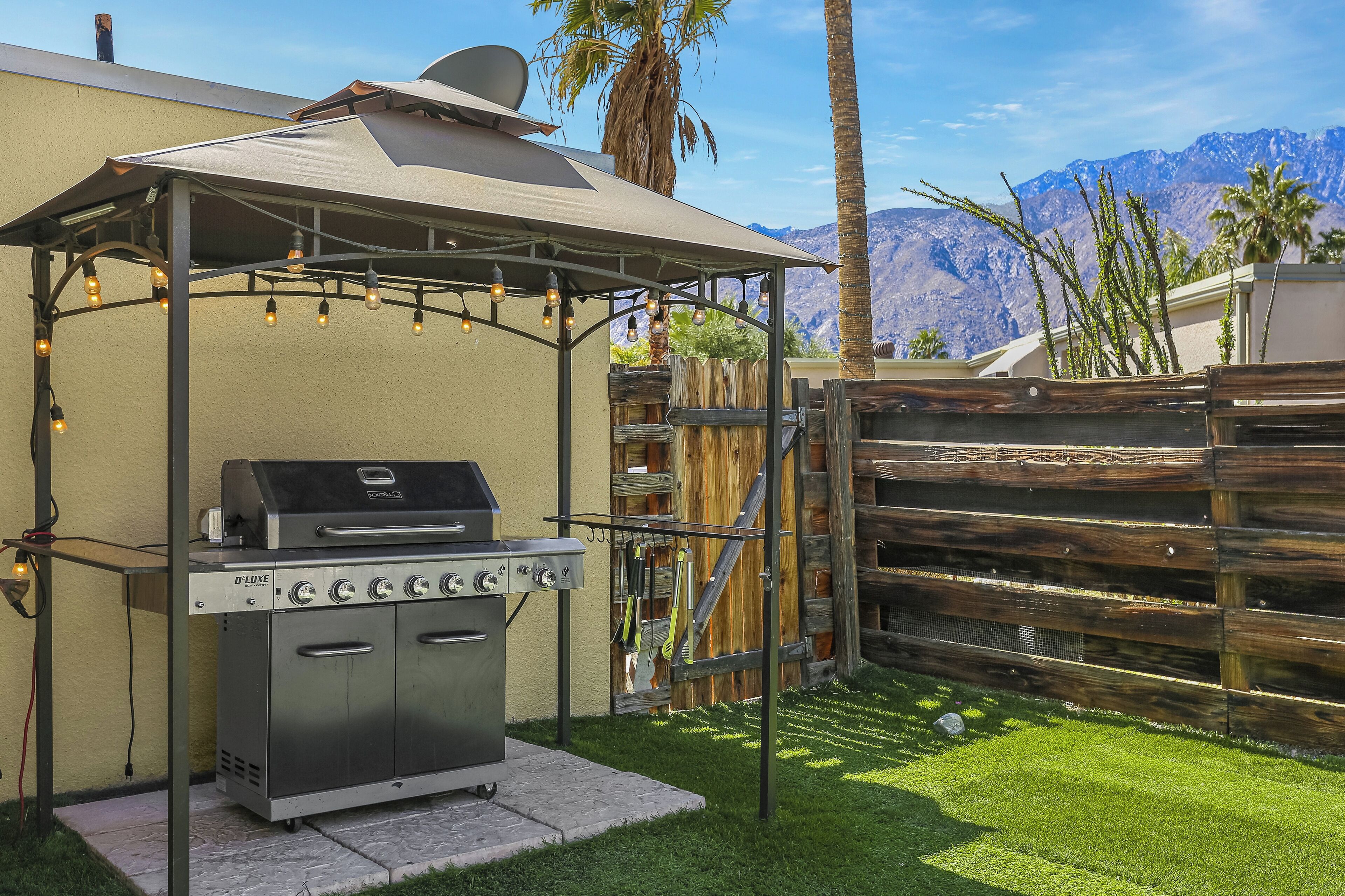 Een buitenbarbecueplaats met een pergola en lichtslingers, met op de achtergrond bergen en palmbomen.