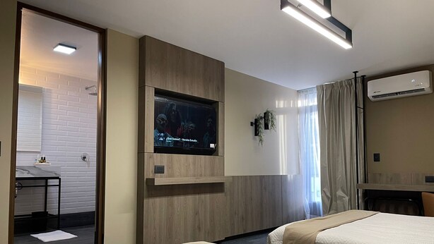 A hotel room with two beds, a TV mounted on the wall, a small desk with a chair, and an air conditioning unit. - Exclusive 409 (Aguascalientes)