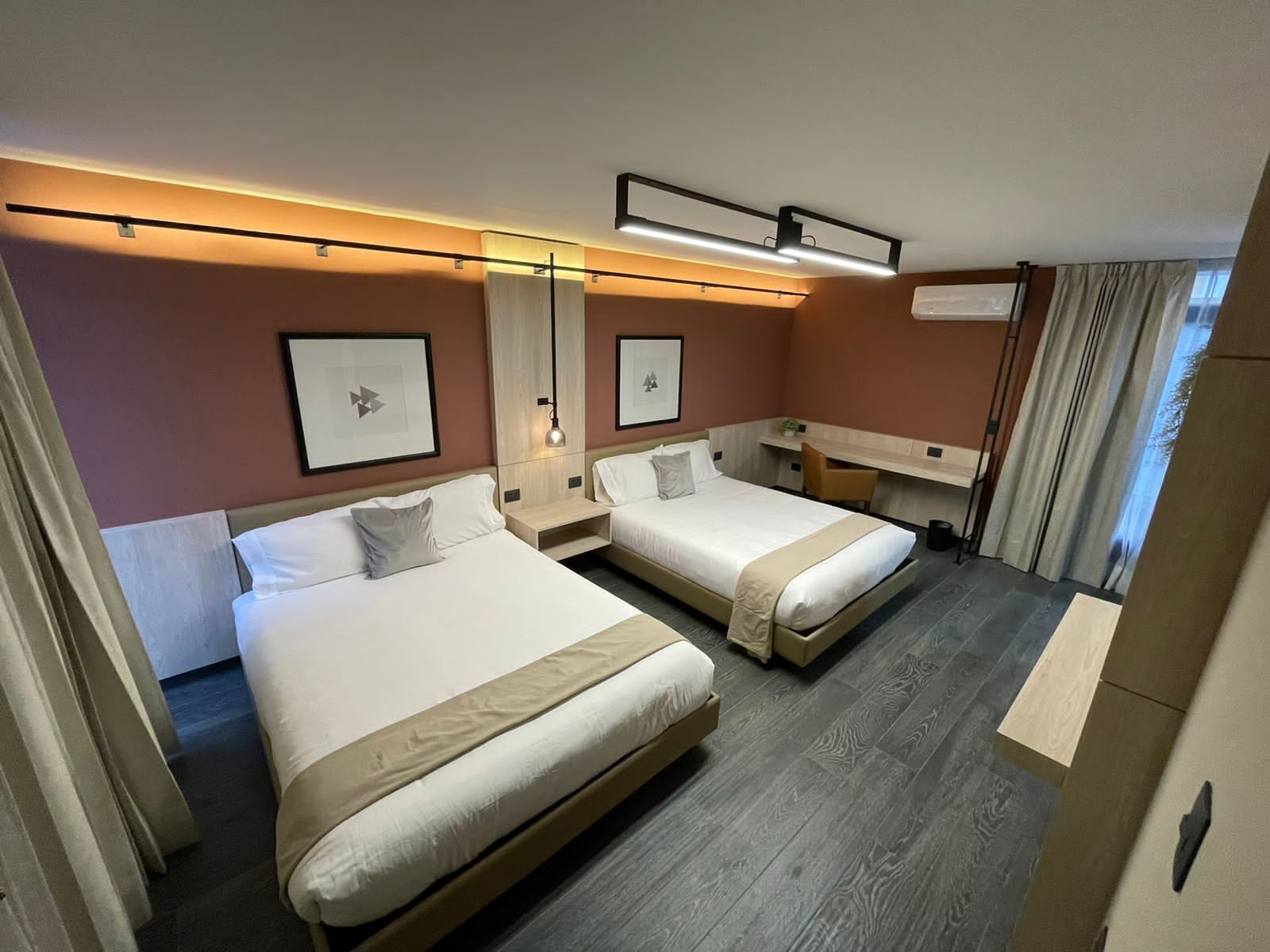 Et hotelværelse med to senge, et skrivebord og et stort vindue.