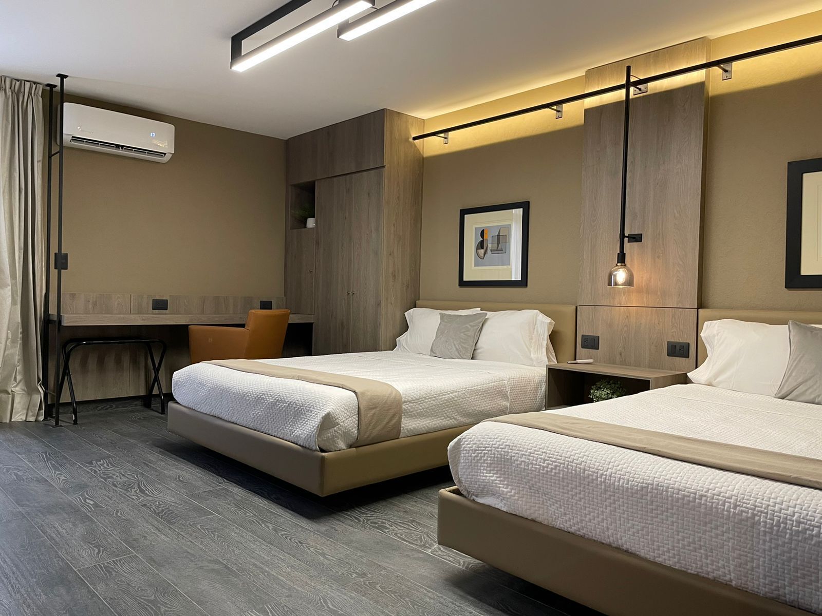 A modern hotel room with two beds, a desk, and a chair.