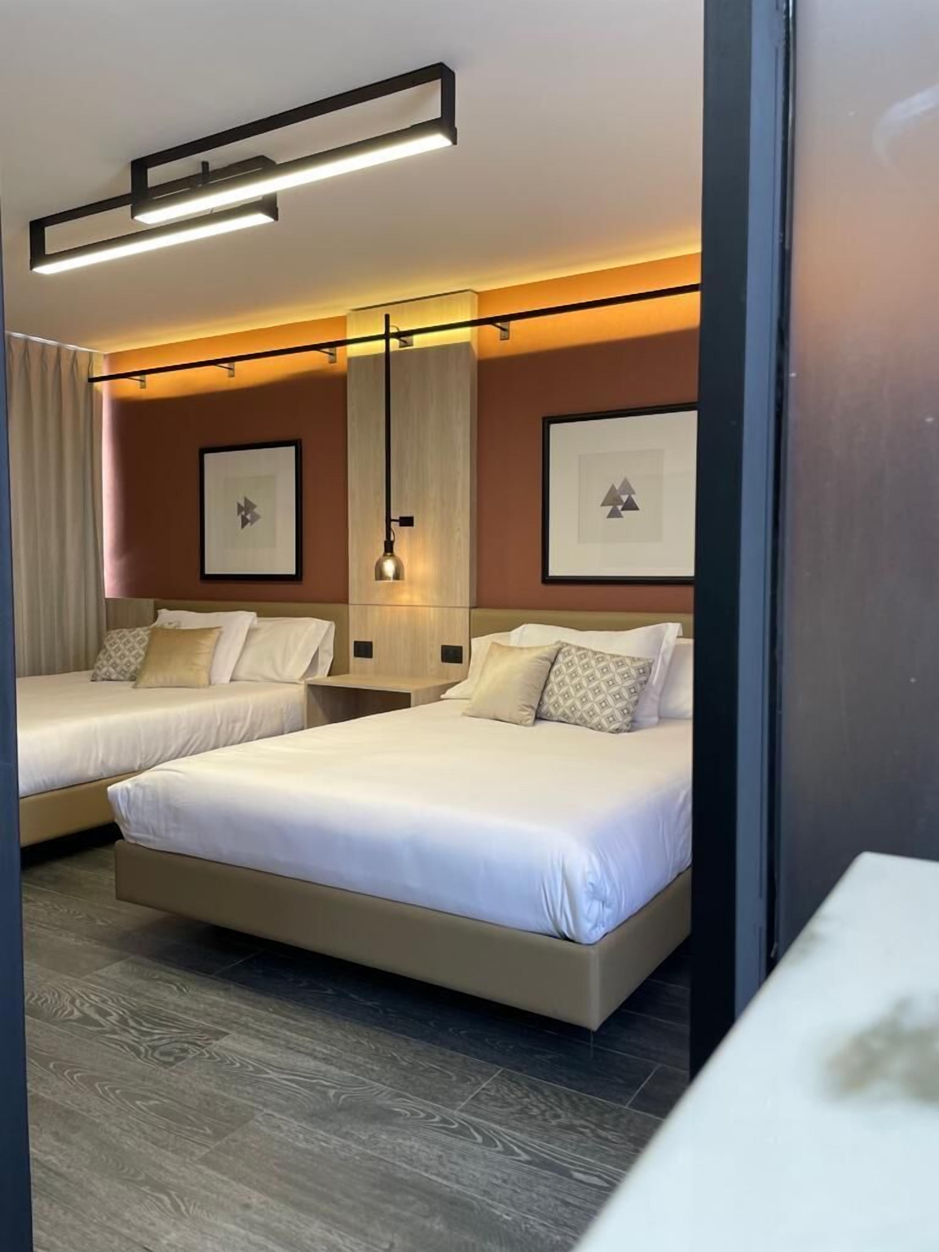 A hotel room with two beds, a large mirror, and framed artwork on the walls.