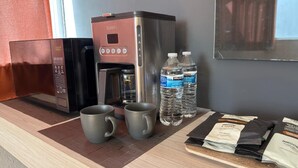 A kitchenette with a coffee maker, two mugs, water bottles, and packaged food items. - Exclusive 409 (Aguascalientes)