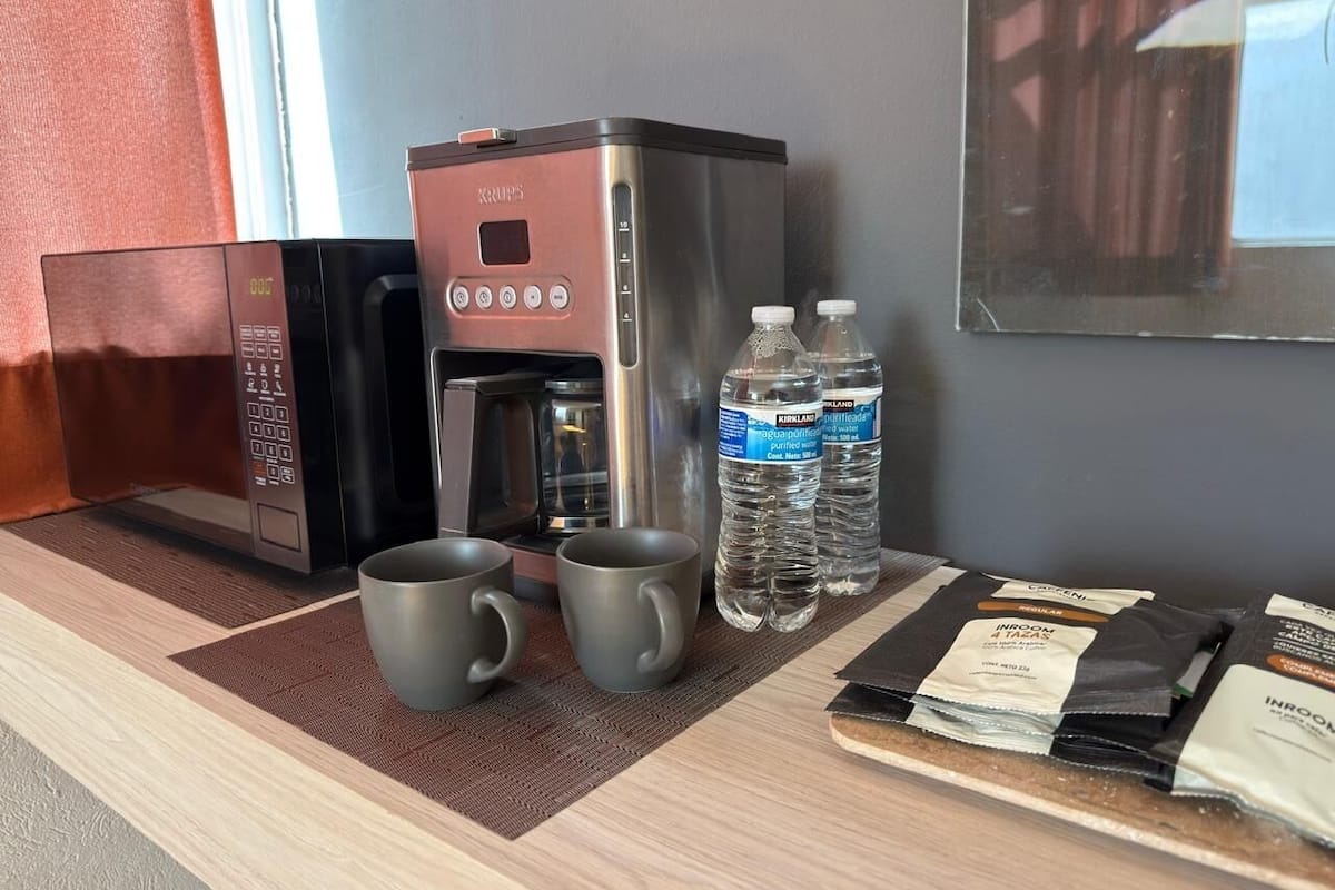 Une petite cuisine équipée d’une machine à café, de deux tasses, de bouteilles d’eau et de produits alimentaires emballés.