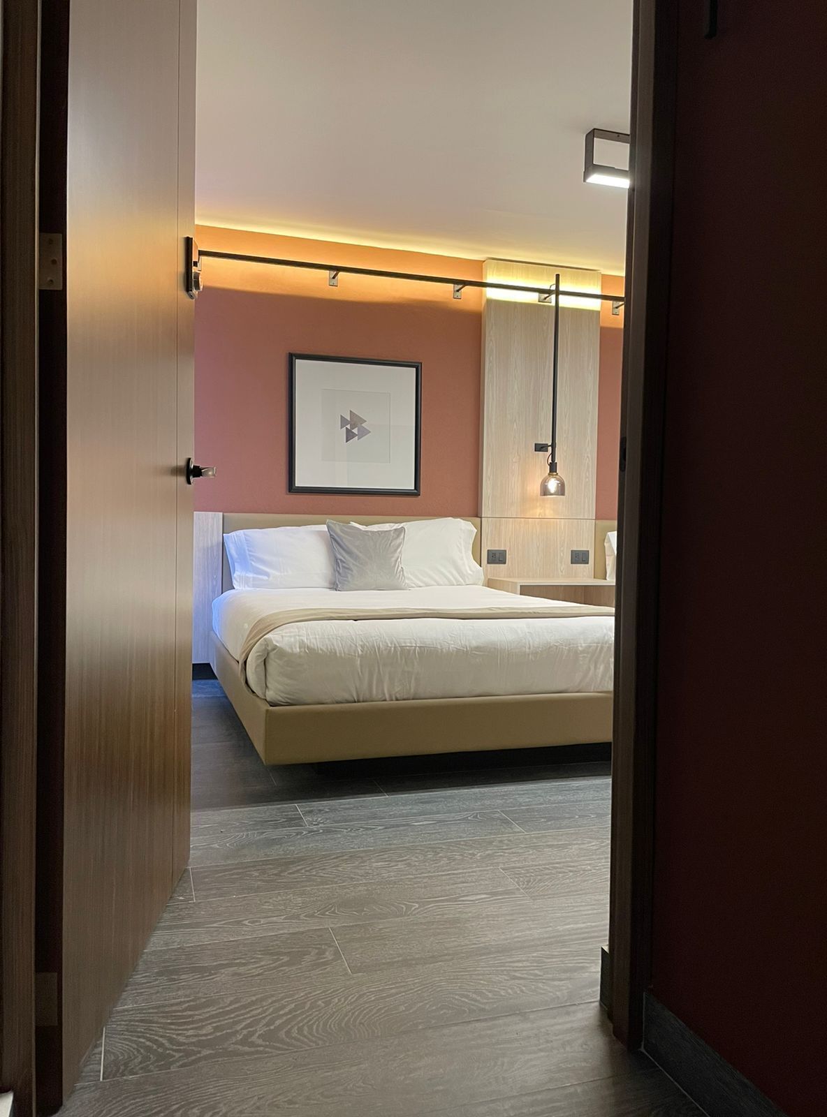 A hotel room with a bed, a bedside table, a lamp, and a framed picture on the wall.