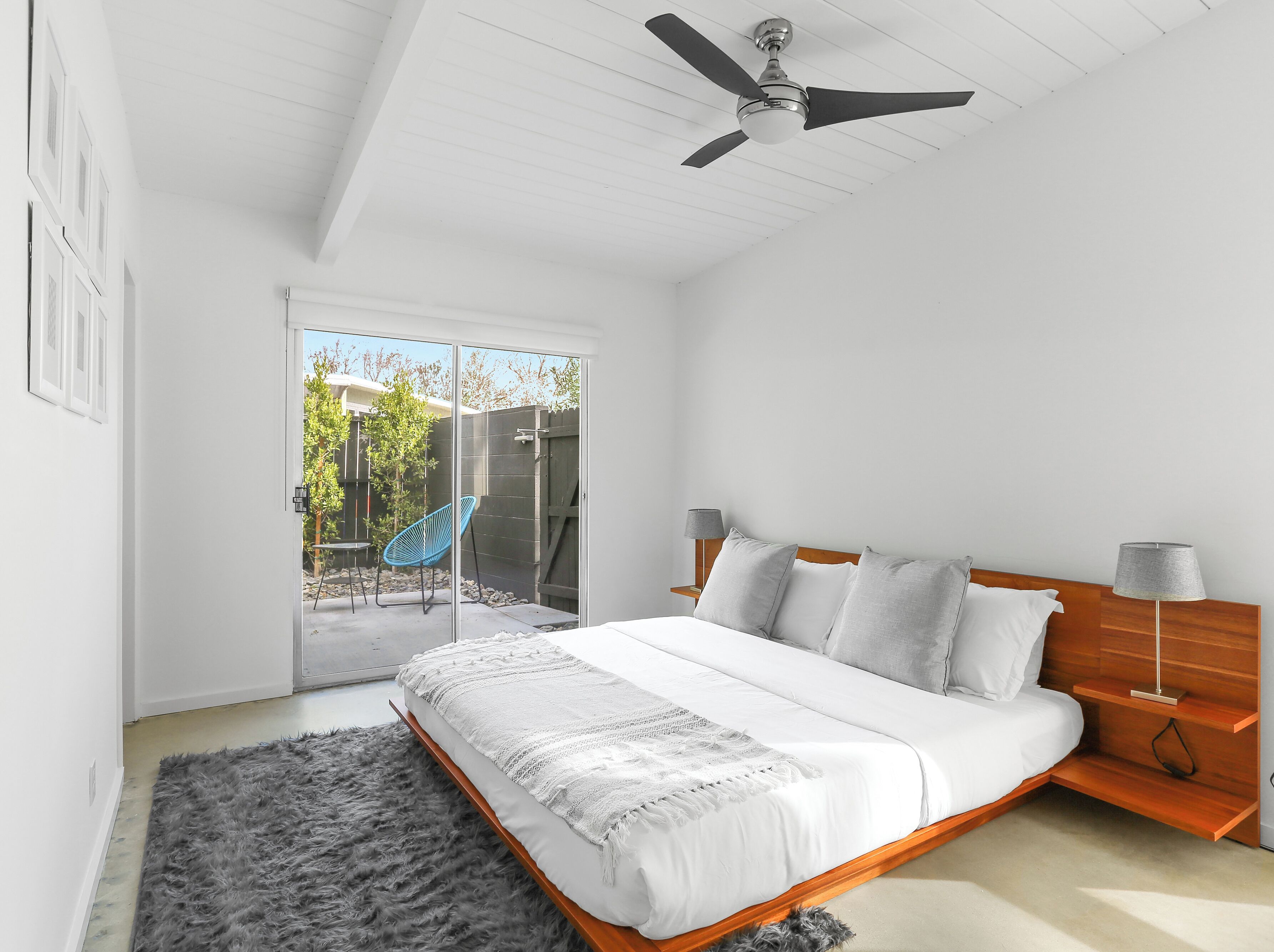 A bedroom with a bed, a ceiling fan, a nightstand, and a view of the outdoors.