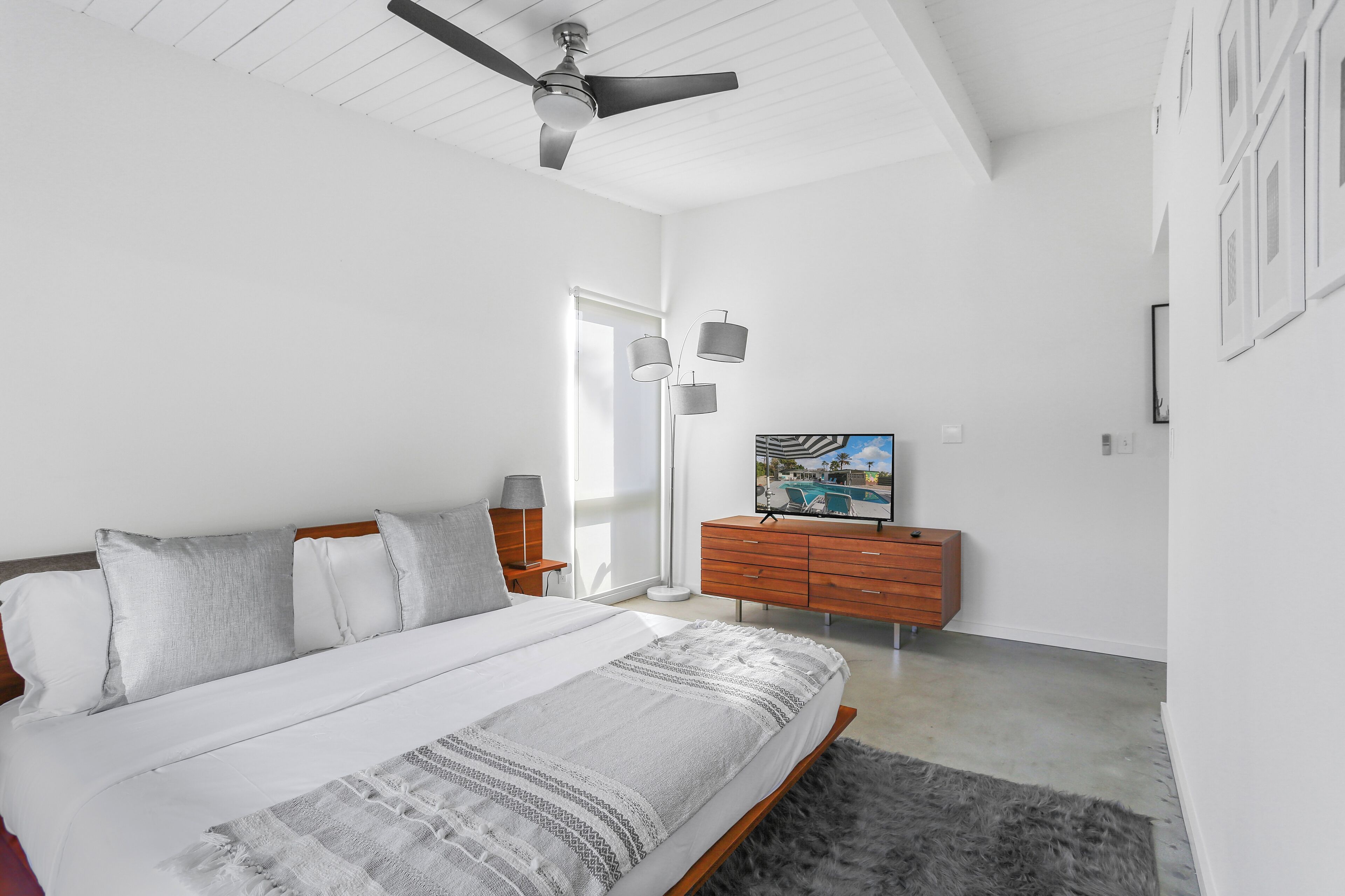 A bedroom with a bed, a ceiling fan, a dresser, and a TV.