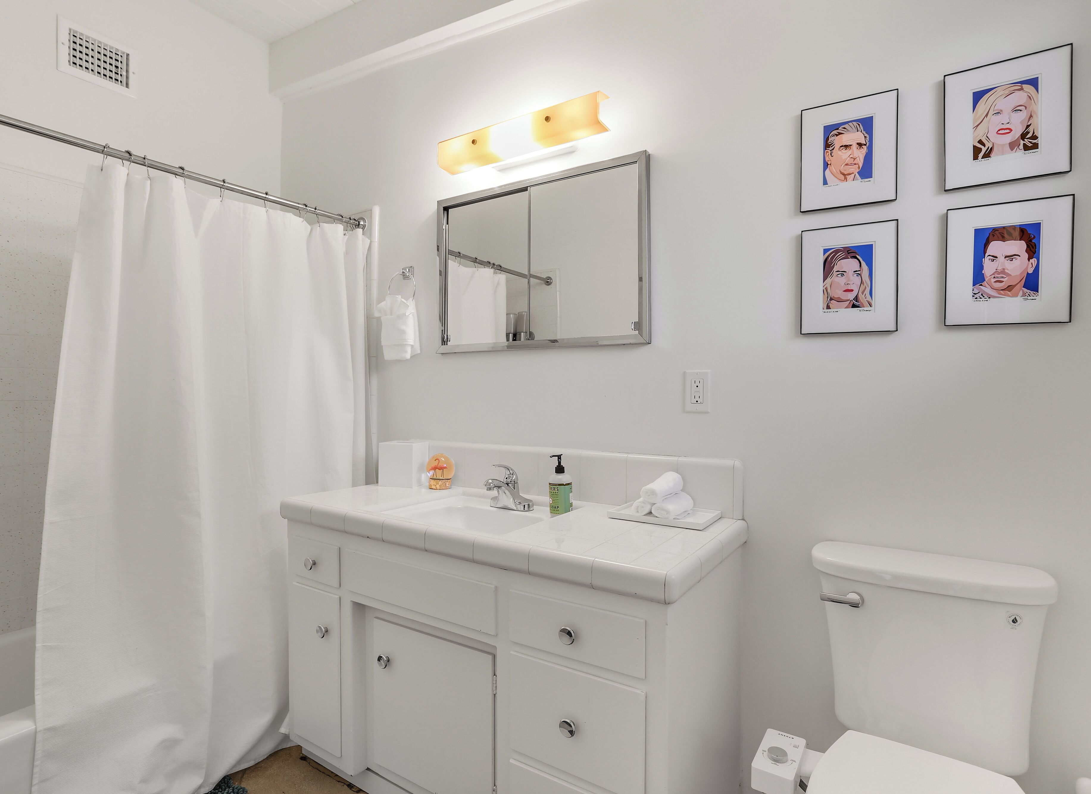 A bathroom with a white sink, mirror, and toilet. There are framed pictures on the wall and a shower curtain.