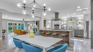 Une cuisine moderne dotée d’un îlot central, d’appareils électroménagers en acier inoxydable et d’un coin repas avec des chaises bleues et une table blanche.