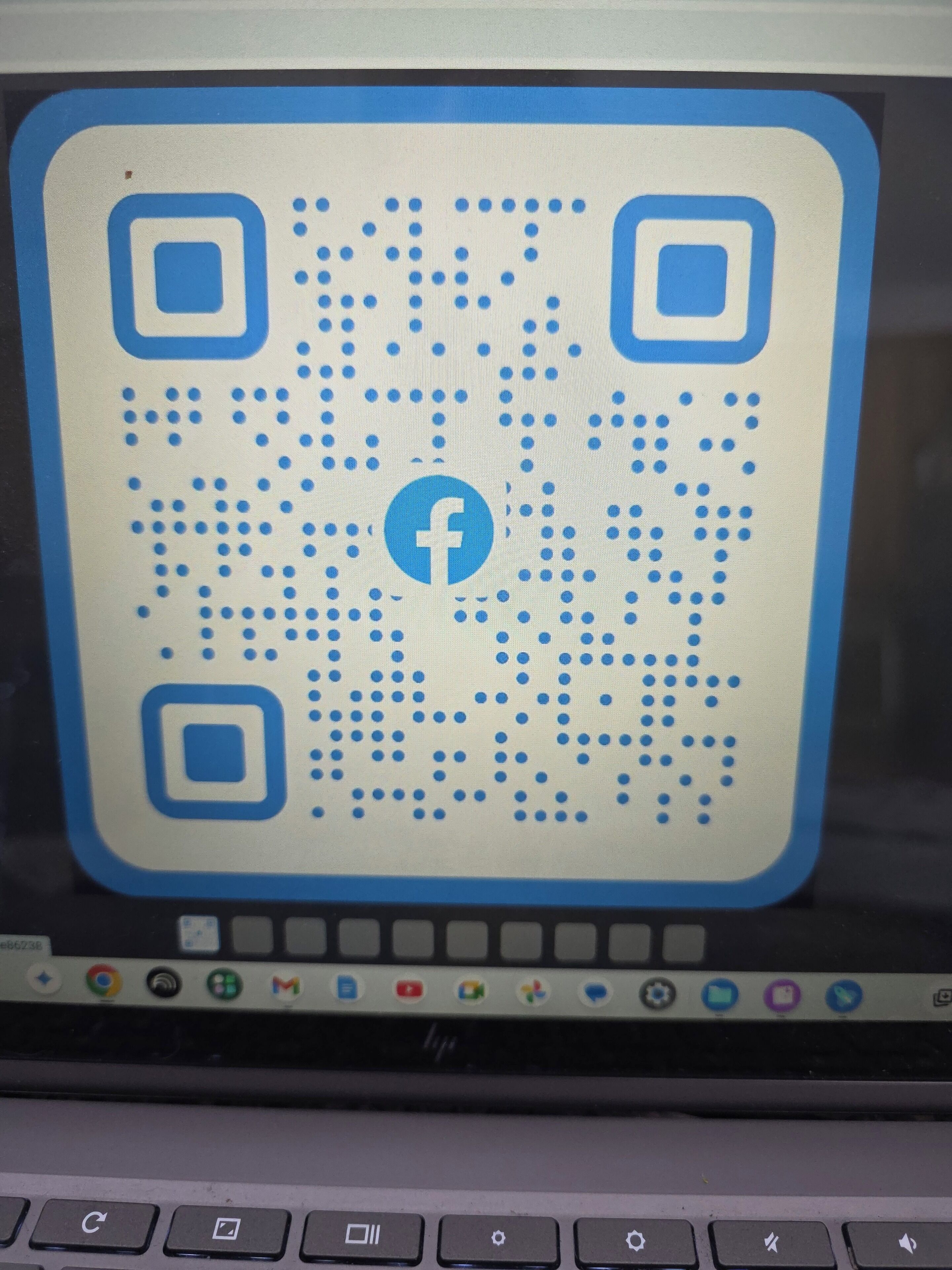 A laptop screen displaying a QR code with a Facebook logo.