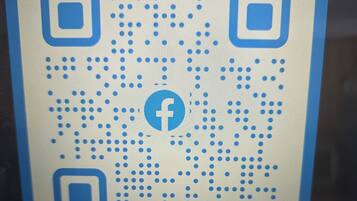 A laptop screen displaying a QR code with a Facebook logo.