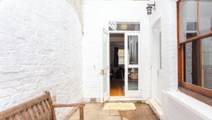 A narrow white brick corridor with a wooden bench, a door leading inside, and a window on the right. - Charming & Peaceful 1BD Home in Camden Town (London)