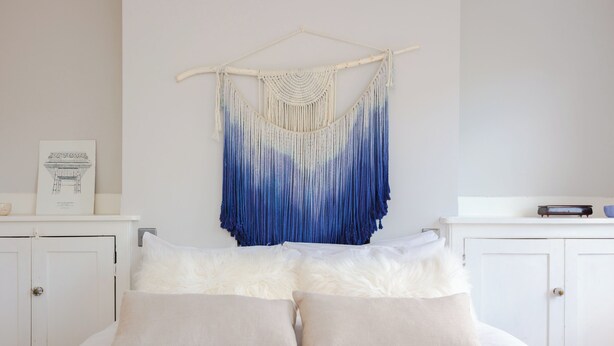 A bedroom with a bed, white pillows, and a macrame wall hanging. - Charming & Peaceful 1BD Home in Camden Town (London)