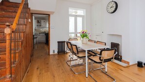 A dining area with a wooden staircase, a white table with chairs, a clock on the wall, and a window with a view. - Charming & Peaceful 1BD Home in Camden Town (London)