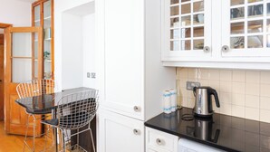 A kitchen with white cabinets, a black countertop, a kettle, and a chair. - Charming & Peaceful 1BD Home in Camden Town (London)