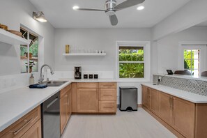 A modern kitchen with wooden cabinets, a dishwasher, a coffee maker, and a trash bin.